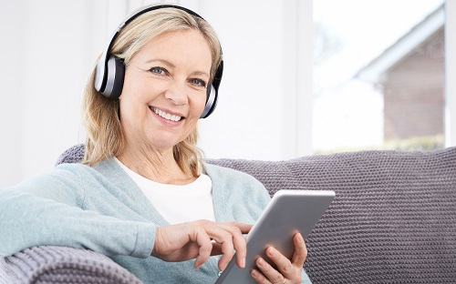 Een lachende vrouw beluistert de Audiokrant via tablet.